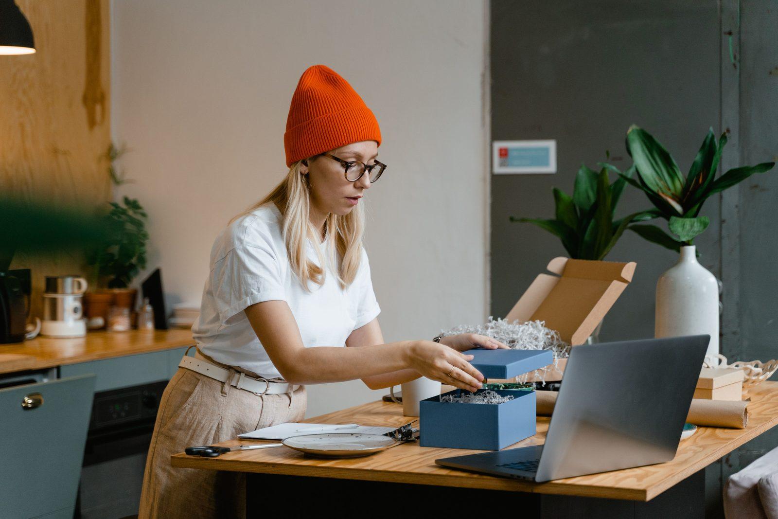 D2C seller packing an order at a desk and booking a courier pickup on a laptop